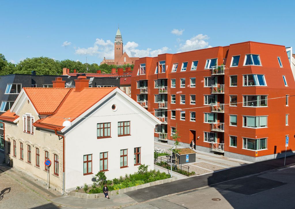 Ett äldre hus står bredvid ett nytt, rött hus där de två översta våningarna har sneda väggar