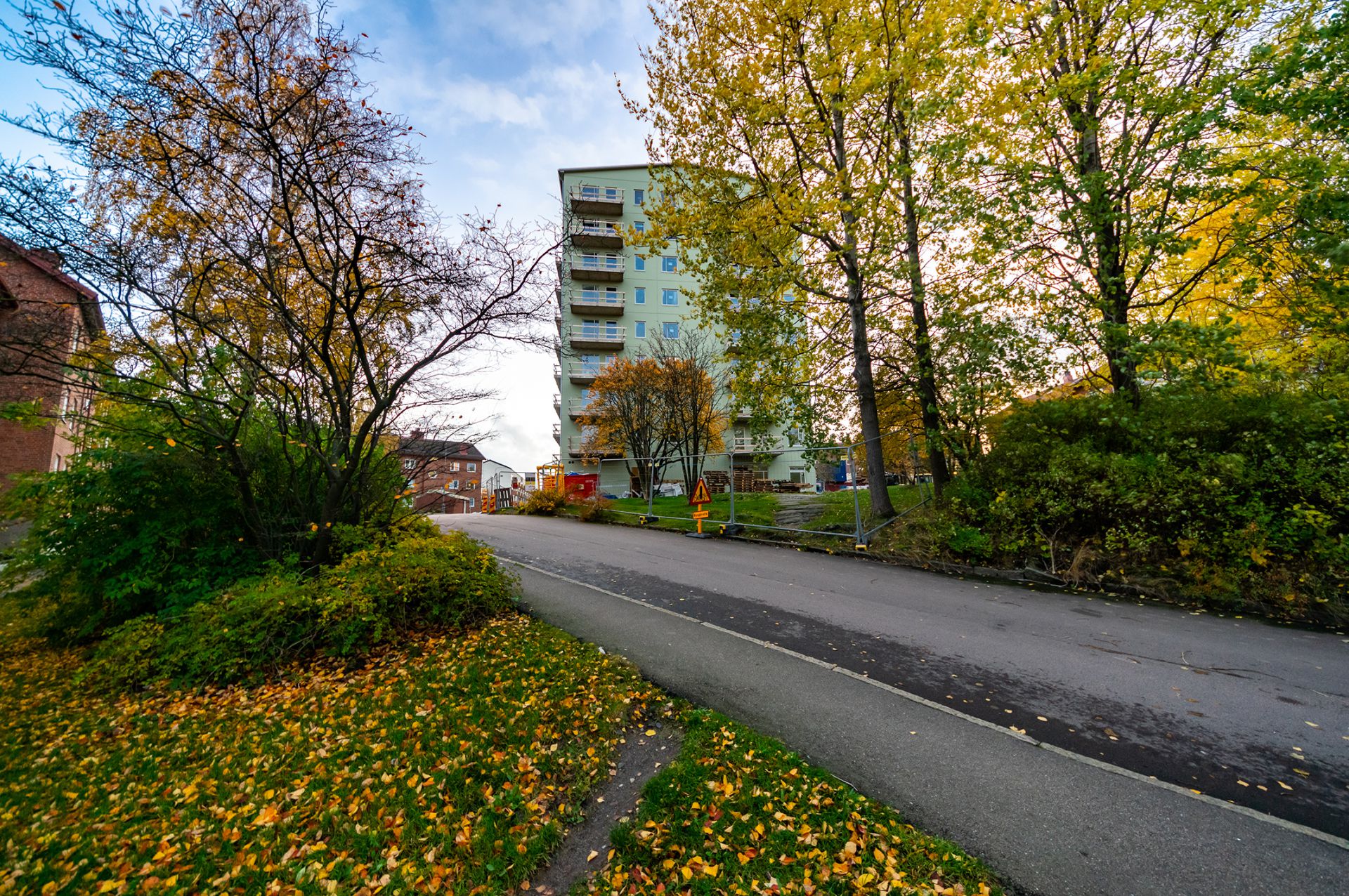 Bild på en uppförsbacke med ett bostadshus som skymtas bakom träden